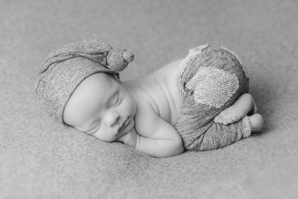 black and white newborn boy posed on a blanket with a hat