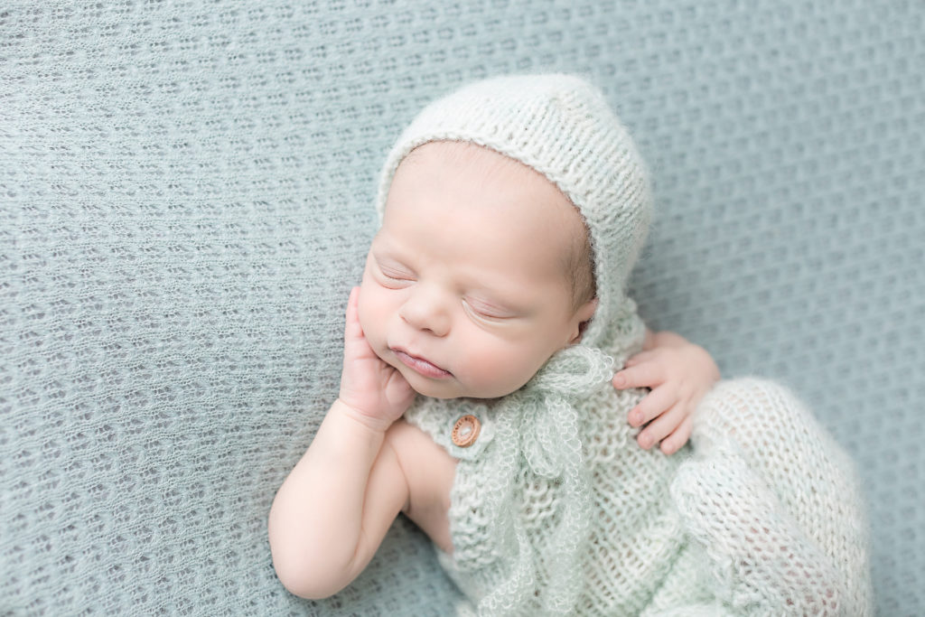Baby with a light green knitted hat posed on a light green blanket