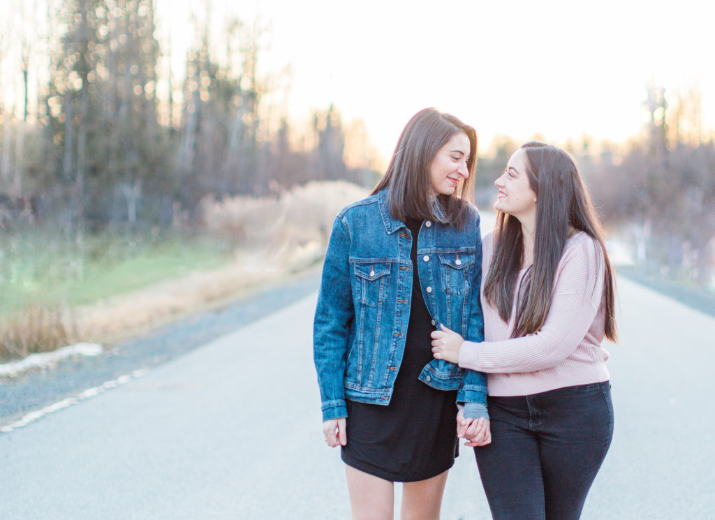 same sex lesbian engagement session during sunset, cute couple very much in love, jean jacket and pink sweater holding hands and walking on the road