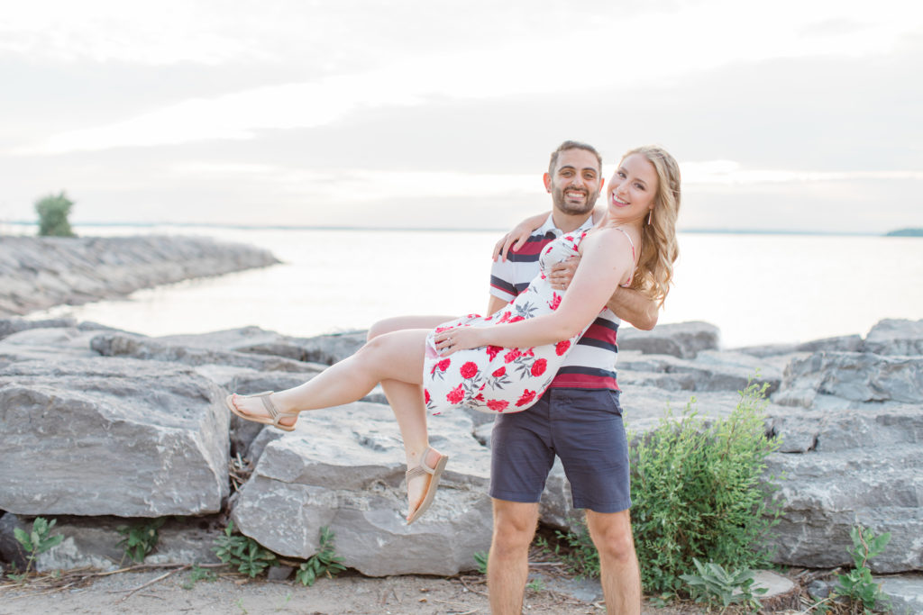 Cute Poses on the beach-  Lift and Twirl - Ideas for what to wear for Engagement Photography, Modern Engagement Session Inspiration Wardrobe Ideas. Unsure of what to wear for your engagement photos, we've got you! Romantic floral dress. Navy, Burgundy, & White T-shirt Polo & Navy shorts . Boat Shoes and Fancy. beaded sandals. Engagement at Britannia Beach, Nepean. Grey Loft Studio is Ottawa's Wedding and Engagement Photographer Videographer for Real couples, showcasing photos that are modern, bright, and fun.