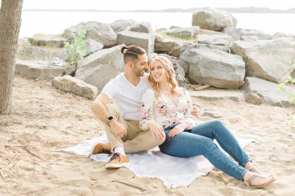 Sitting on the Beach - Ideas for what to wear for Engagement Photography, Modern Engagement Session Inspiration Wardrobe Ideas. Unsure of what to wear for your engagement photos, we've got you! Romantic floral shirt & jeans.  White T-shirt & neutral pants . Boat Shoes and Fancy. beaded sandals. Engagement at Petrie Island, Orleans. Grey Loft Studio is Ottawa's Wedding and Engagement Photographer Videographer for Real couples, showcasing photos that are modern, bright, and fun.