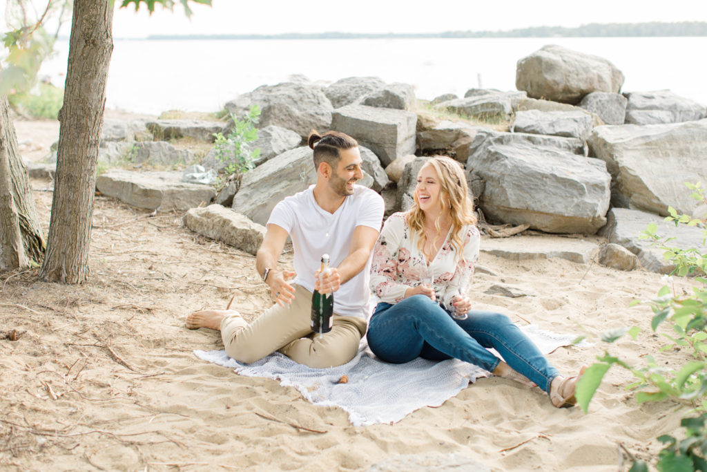 Laughing together - Sitting on the Beach - Ideas for what to wear for Engagement Photography, Modern Engagement Session Inspiration Wardrobe Ideas. Unsure of what to wear for your engagement photos, we've got you! Romantic floral shirt & jeans.  White T-shirt & neutral pants . Boat Shoes and Fancy. beaded sandals. Engagement at Petrie Island, Orleans. Grey Loft Studio is Ottawa's Wedding and Engagement Photographer Videographer for Real couples, showcasing photos that are modern, bright, and fun.