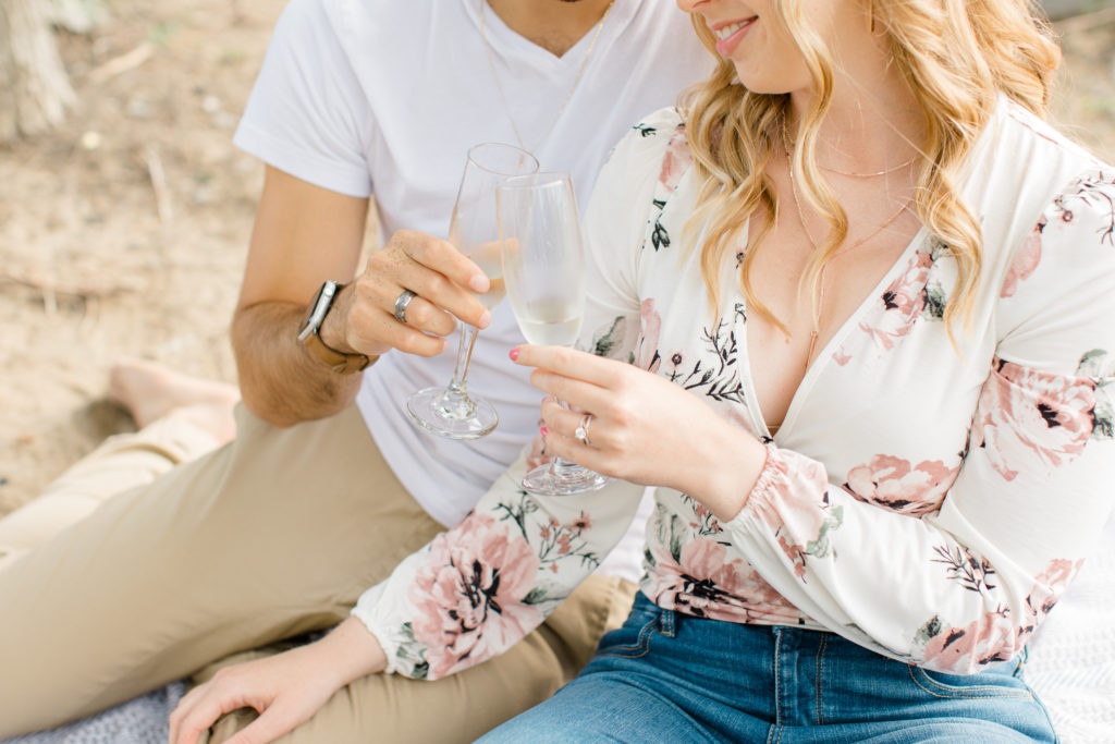 Cheers Photo - Sitting on the Beach - Ideas for what to wear for Engagement Photography, Modern Engagement Session Inspiration Wardrobe Ideas. Unsure of what to wear for your engagement photos, we've got you! Romantic floral shirt & jeans.  White T-shirt & neutral pants . Boat Shoes and Fancy. beaded sandals. Engagement at Petrie Island, Orleans. Grey Loft Studio is Ottawa's Wedding and Engagement Photographer Videographer for Real couples, showcasing photos that are modern, bright, and fun.