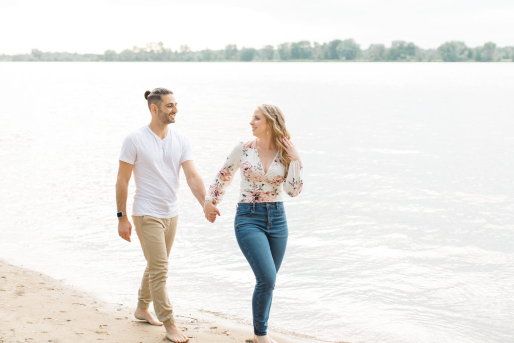 Walking on the beach - Ideas for what to wear for Engagement Photography, Modern Engagement Session Inspiration Wardrobe Ideas. Unsure of what to wear for your engagement photos, we've got you! Romantic floral shirt & jeans.  White T-shirt & neutral pants . Boat Shoes and Fancy. beaded sandals. Engagement at Petrie Island, Orleans. Grey Loft Studio is Ottawa's Wedding and Engagement Photographer Videographer for Real couples, showcasing photos that are modern, bright, and fun.