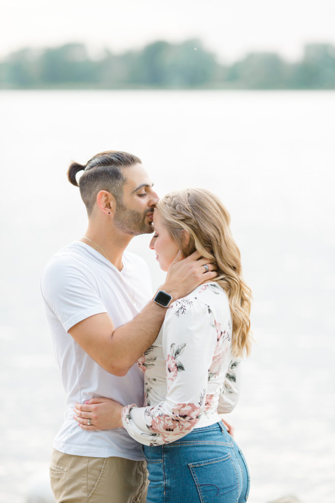 Forehead Kiss on the Beach - Ideas for what to wear for Engagement Photography, Modern Engagement Session Inspiration Wardrobe Ideas. Unsure of what to wear for your engagement photos, we've got you! Romantic floral shirt & jeans.  White T-shirt & neutral pants . Boat Shoes and Fancy. beaded sandals. Engagement at Petrie Island, Orleans. Grey Loft Studio is Ottawa's Wedding and Engagement Photographer Videographer for Real couples, showcasing photos that are modern, bright, and fun.