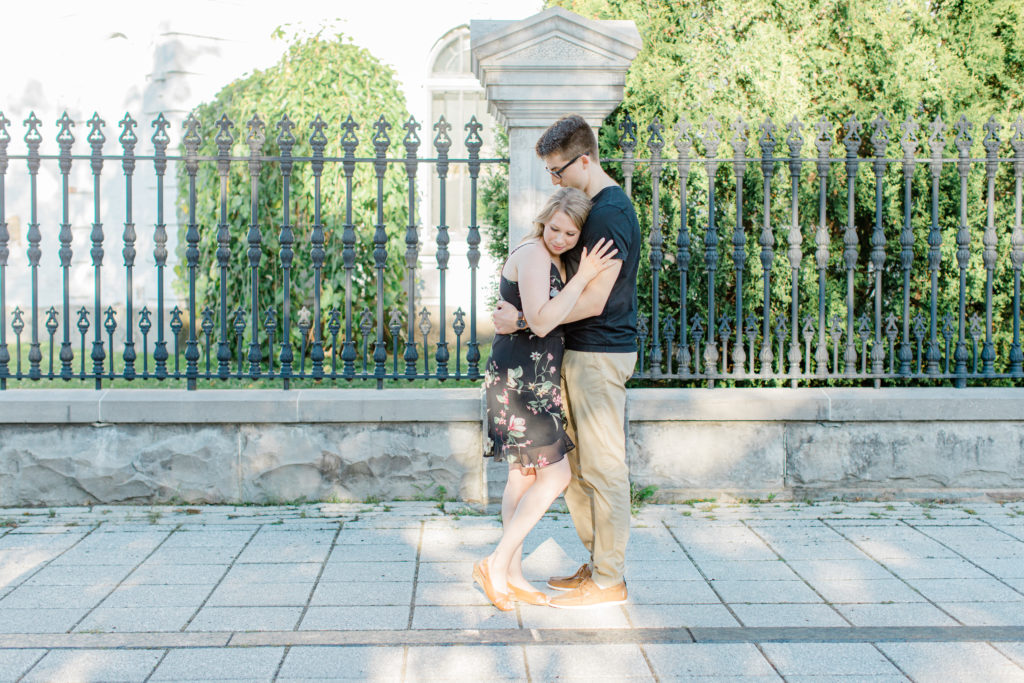 Hugging Photos - Standing at Rideau Hall - Ideas for what to wear for Engagement Photography, Modern Engagement Session Inspiration Wardrobe Ideas. Unsure of what to wear for your engagement photos, we've got you! Romantic floral dress. Black Polo T-shirt & neutral pants . Boat Shoes and Fancy beaded wedges. Engagement downtown Ottawa. Grey Loft Studio is Ottawa's Wedding and Engagement Photographer Videographer for Real couples, showcasing photos that are modern, bright, and fun.