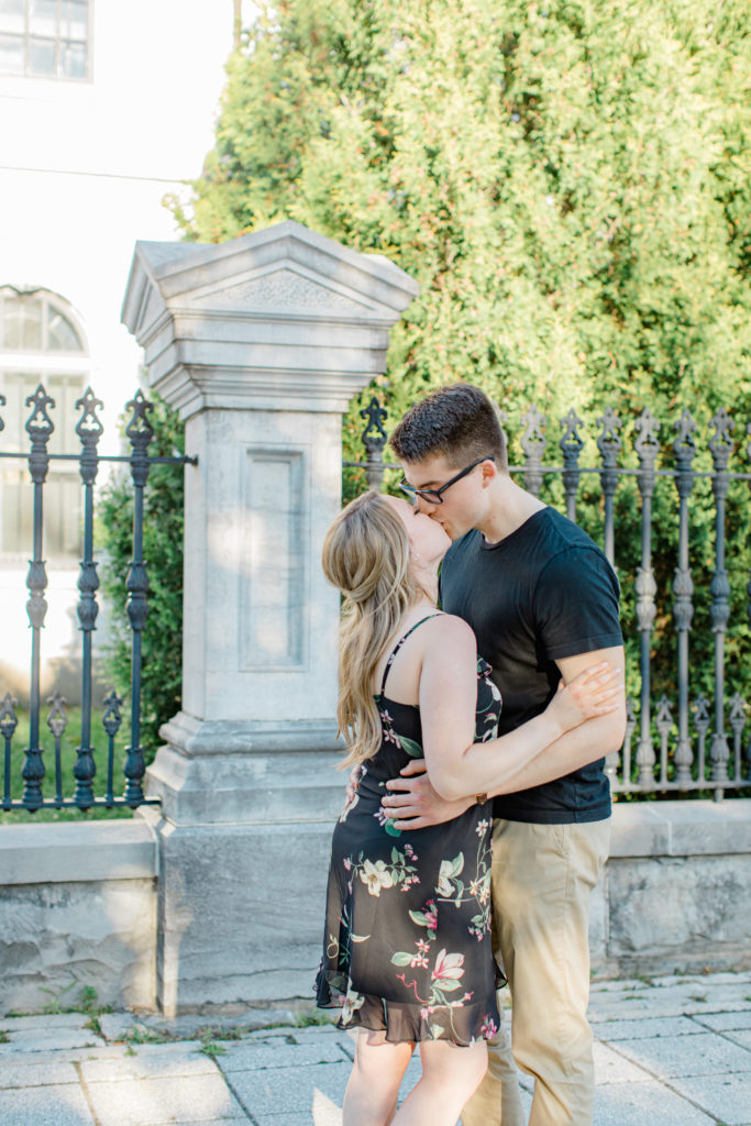 Kissing while Standing at Rideau Hall - Ideas for what to wear for Engagement Photography, Modern Engagement Session Inspiration Wardrobe Ideas. Unsure of what to wear for your engagement photos, we've got you! Romantic floral dress. Black Polo T-shirt & neutral pants . Boat Shoes and Fancy beaded wedges. Engagement downtown Ottawa. Grey Loft Studio is Ottawa's Wedding and Engagement Photographer Videographer for Real couples, showcasing photos that are modern, bright, and fun.