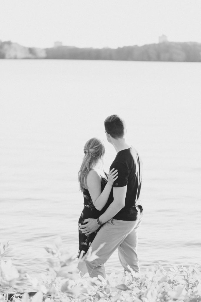Looking out into Water - Romantic Posing - Cute Posing for Tall guys with short girls - Engagement Photo Poses- Posing close to Rideau Hall - Ideas for what to wear for Engagement Photography, Modern Engagement Session Inspiration Wardrobe Ideas. Unsure of what to wear for your engagement photos, we've got you! Romantic floral dress. Black Polo T-shirt & neutral pants . Boat Shoes and Fancy beaded wedges. Engagement downtown Ottawa. Grey Loft Studio is Ottawa's Wedding and Engagement Photographer Videographer for Real couples, showcasing photos that are modern, bright, and fun. Photographe Gatineau -Posing on the Ottawa River