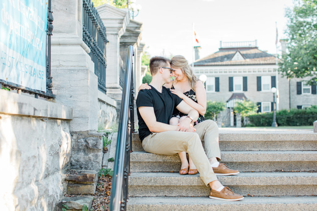 Cute couple Posing while sitting on steps at Rideau Hall - Ideas for what to wear for Engagement Photography, Modern Engagement Session Inspiration Wardrobe Ideas. Unsure of what to wear for your engagement photos, we've got you! Romantic floral dress. Black Polo T-shirt & neutral pants . Boat Shoes and Fancy beaded wedges. Engagement downtown Ottawa. Grey Loft Studio is Ottawa's Wedding and Engagement Photographer Videographer for Real couples, showcasing photos that are modern, bright, and fun.