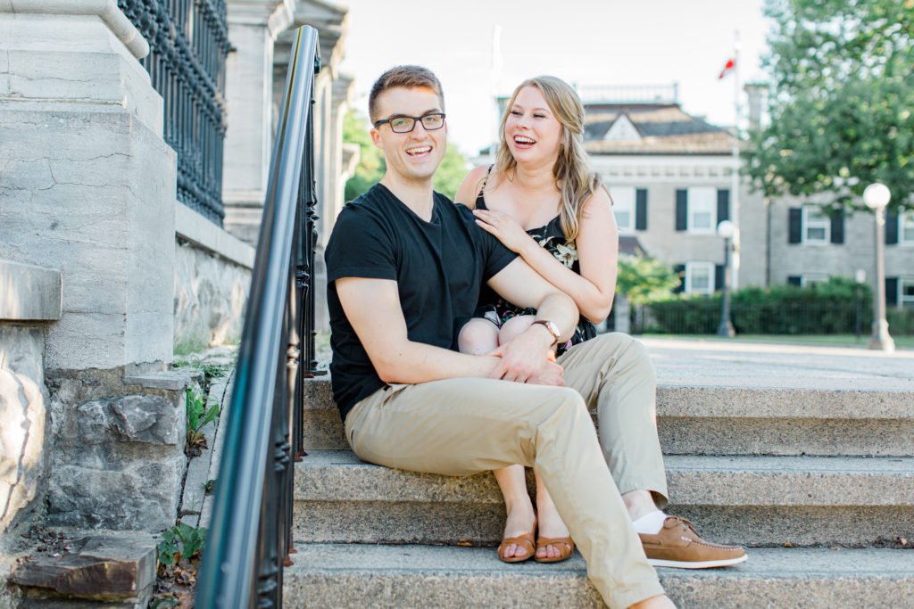 Cute couple Posing while sitting on steps at Rideau Hall - Ideas for what to wear for Engagement Photography, Modern Engagement Session Inspiration Wardrobe Ideas. Unsure of what to wear for your engagement photos, we've got you! Romantic floral dress. Black Polo T-shirt & neutral pants . Boat Shoes and Fancy beaded wedges. Engagement downtown Ottawa. Grey Loft Studio is Ottawa's Wedding and Engagement Photographer Videographer for Real couples, showcasing photos that are modern, bright, and fun.