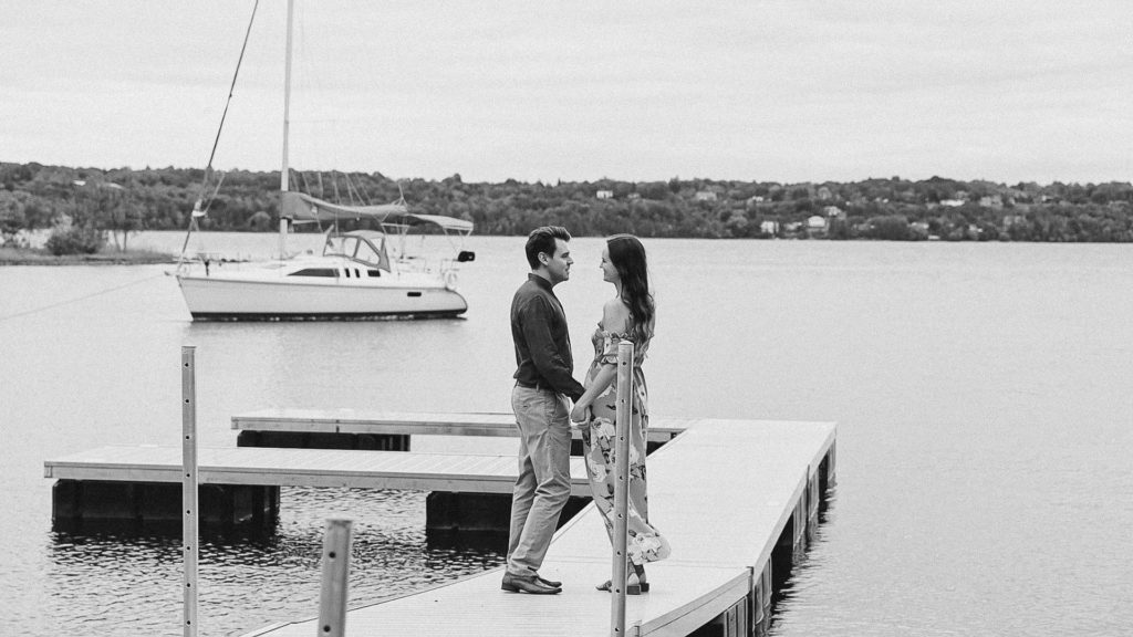 Standing on Dock - Couple- in Black and White-Ideas for what to wear for Engagement Photography, Modern Engagement Session Inspiration Wardrobe Ideas. Unsure of what to wear for your engagement photos, we've got you! Romantic white with Pink Flower dress for Summer Engagement in Ottawa. Grey Loft Studio is Ottawa's Wedding and Engagement Photographer for Real couples, showcasing photos that are modern, bright, and fun.