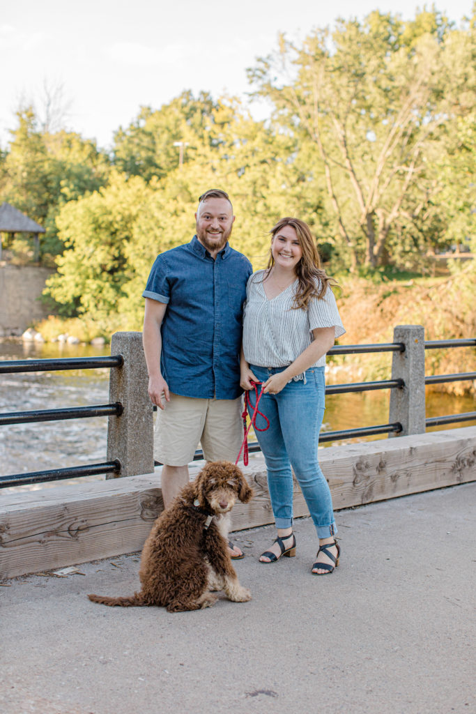Chocolate Golden Doodle Puppy - grey loft studio - Couple holding each other close and walking looking back -engagement session - Watson's Mill Engagement Session Manotick - Bright & Airy photography - Grey Loft Studio - Ottawa Wedding Photographer - Ottawa Wedding Videographer - Engagement Session Locations in Ottawa - Summer Engagement session - Light blue and Cream with casual jeans and strap sandals. Ottawa Photo Studio.