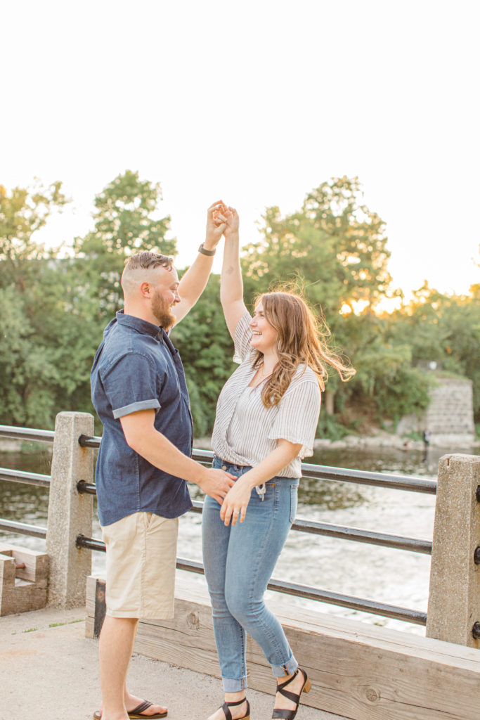Dancing during engagement session - Watson's Mill Engagement Session Manotick - Bright & Airy photography - Grey Loft Studio - Ottawa Wedding Photographer - Ottawa Wedding Videographer - Engagement Session Locations in Ottawa - Summer Engagement session - Light blue and Cream with casual jeans and strap sandals. Ottawa Photo Studio.