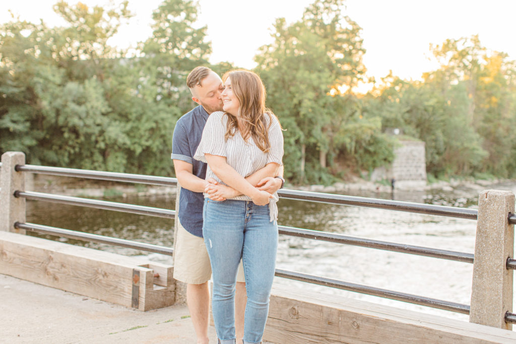 Cute pose on a Bridge at Sunset - Watson's Mill Engagement Session Manotick - Bright & Airy photography - Grey Loft Studio - Ottawa Wedding Photographer - Ottawa Wedding Videographer - Engagement Session Locations in Ottawa - Summer Engagement session - Light blue and Cream with casual jeans and strap sandals. Ottawa Photo Studio.