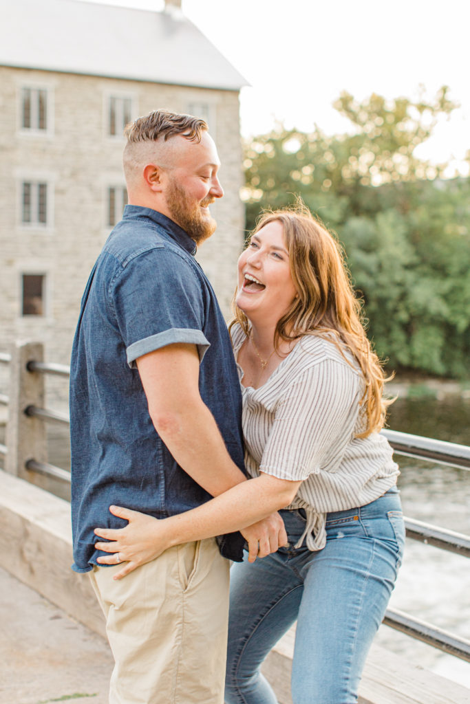 Couple having fun during engagement session - Watson's Mill Engagement Session Manotick - Bright & Airy photography - Grey Loft Studio - Ottawa Wedding Photographer - Ottawa Wedding Videographer - Engagement Session Locations in Ottawa - Summer Engagement session - Light blue and Cream with casual jeans and strap sandals. Ottawa Photo Studio.
