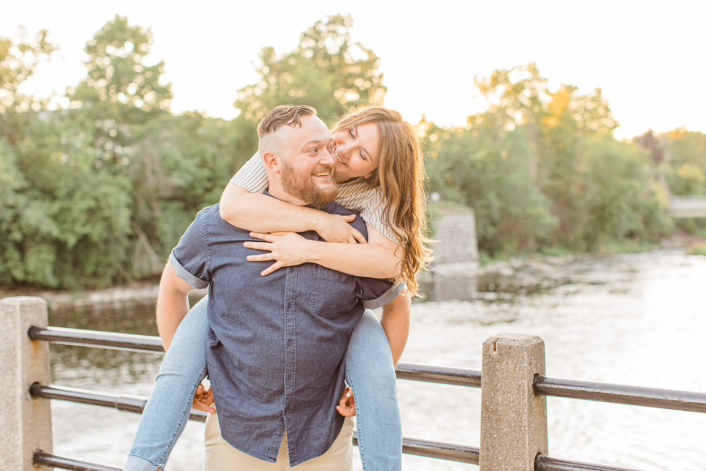 Piggy Back Pose during Engagement Session - Watson's Mill Engagement Session Manotick - Bright & Airy photography - Grey Loft Studio - Ottawa Wedding Photographer - Ottawa Wedding Videographer - Engagement Session Locations in Ottawa - Summer Engagement session - Light blue and Cream with casual jeans and strap sandals. Ottawa Photo Studio.