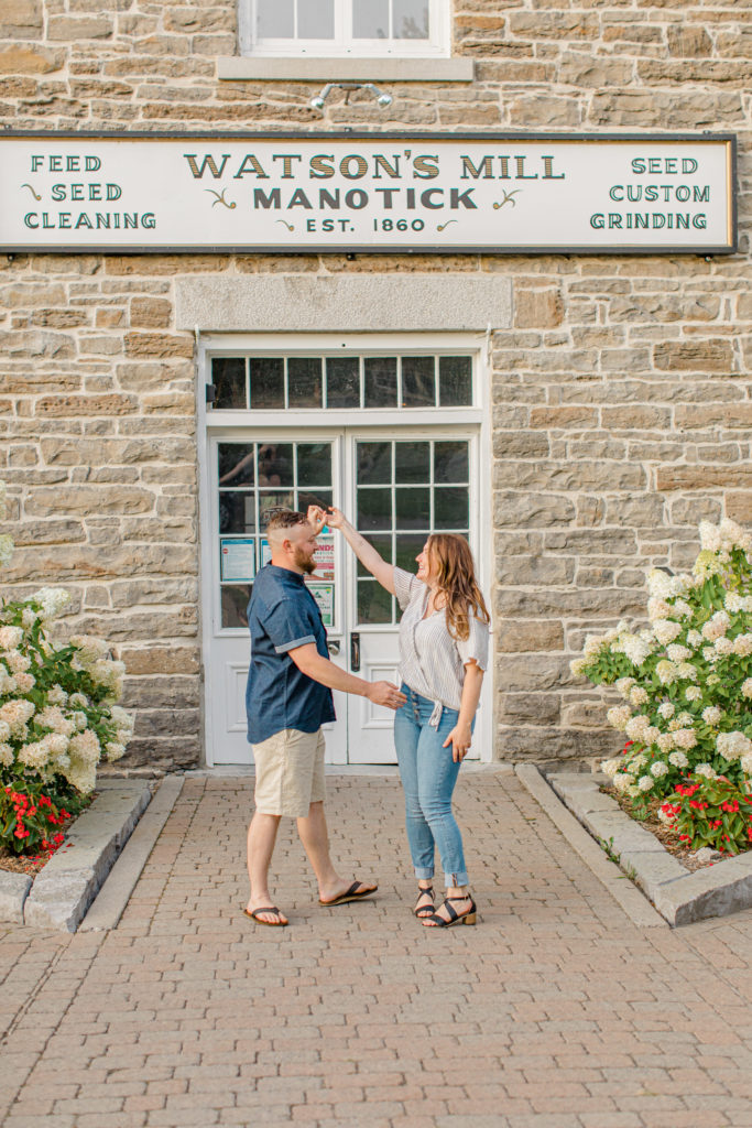 Spinning during engagement Session - Watson's Mill Engagement Session Manotick - Bright & Airy photography - Grey Loft Studio - Ottawa Wedding Photographer - Ottawa Wedding Videographer - Engagement Session Locations in Ottawa - Summer Engagement session - Light blue and Cream with casual jeans and strap sandals. Ottawa Photo Studio.