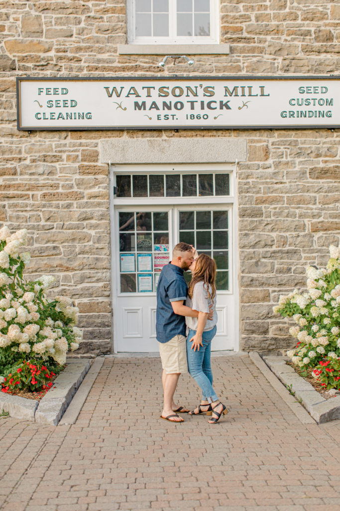 Couple Kissing during engagement session - Watson's Mill Engagement Session Manotick - Bright & Airy photography - Grey Loft Studio - Ottawa Wedding Photographer - Ottawa Wedding Videographer - Engagement Session Locations in Ottawa - Summer Engagement session - Light blue and Cream with casual jeans and strap sandals. Ottawa Photo Studio.