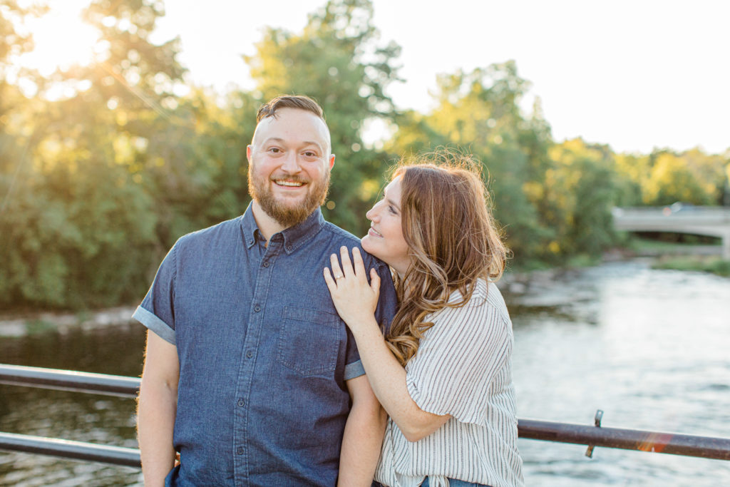Couple holding each other close -engagement session - Watson's Mill Engagement Session Manotick - Bright & Airy photography - Grey Loft Studio - Ottawa Wedding Photographer - Ottawa Wedding Videographer - Engagement Session Locations in Ottawa - Summer Engagement session - Light blue and Cream with casual jeans and strap sandals. Ottawa Photo Studio.