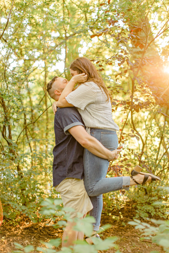 Lift and carry - Couple holding each other close -engagement session - Watson's Mill Engagement Session Manotick - Bright & Airy photography - Grey Loft Studio - Ottawa Wedding Photographer - Ottawa Wedding Videographer - Engagement Session Locations in Ottawa - Summer Engagement session - Light blue and Cream with casual jeans and strap sandals. Ottawa Photo Studio.
