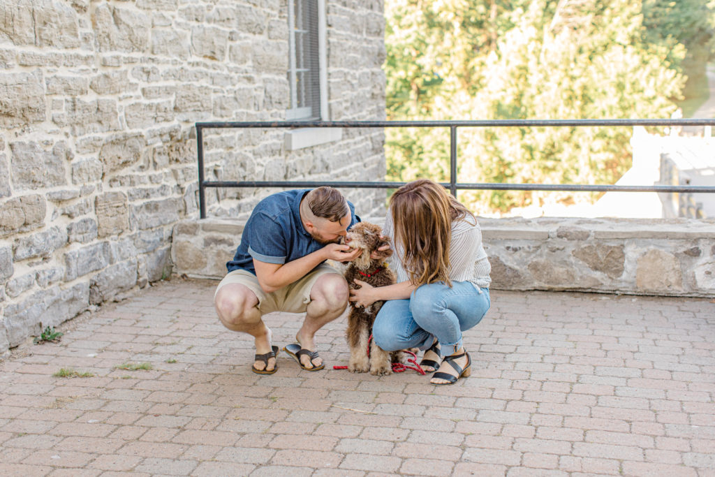 Chocolate Golden Doodle Puppy - grey loft studio - Couple holding each other close and walking looking back -engagement session - Watson's Mill Engagement Session Manotick - Bright & Airy photography - Grey Loft Studio - Ottawa Wedding Photographer - Ottawa Wedding Videographer - Engagement Session Locations in Ottawa - Summer Engagement session - Light blue and Cream with casual jeans and strap sandals. Ottawa Photo Studio.