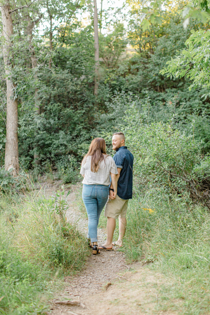 Couple Holding hands during engagement session - Watson's Mill Engagement Session Manotick - Bright & Airy photography - Grey Loft Studio - Ottawa Wedding Photographer - Ottawa Wedding Videographer - Engagement Session Locations in Ottawa - Summer Engagement session - Light blue and Cream with casual jeans and strap sandals. Ottawa Photo Studio.
