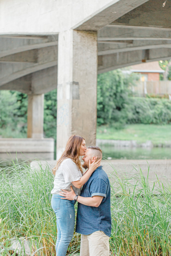Couple kissing - kiss the forehead during engagement session - Watson's Mill Engagement Session Manotick - Bright & Airy photography - Grey Loft Studio - Ottawa Wedding Photographer - Ottawa Wedding Videographer - Engagement Session Locations in Ottawa - Summer Engagement session - Light blue and Cream with casual jeans and strap sandals. Ottawa Photo Studio.
