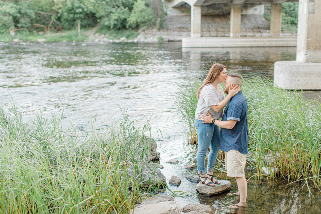 Couple kissing - kiss the forehead during engagement session - Watson's Mill Engagement Session Manotick - Bright & Airy photography - Grey Loft Studio - Ottawa Wedding Photographer - Ottawa Wedding Videographer - Engagement Session Locations in Ottawa - Summer Engagement session - Light blue and Cream with casual jeans and strap sandals. Ottawa Photo Studio.
