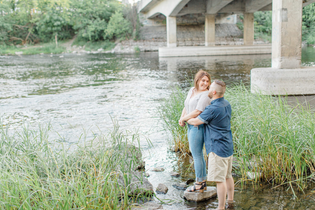 Braving the water - Watson's Mill Engagement Session Manotick - Bright & Airy photography - Grey Loft Studio - Ottawa Wedding Photographer - Ottawa Wedding Videographer - Engagement Session Locations in Ottawa - Summer Engagement session - Light blue and Cream with casual jeans and strap sandals. Ottawa Photo Studio.