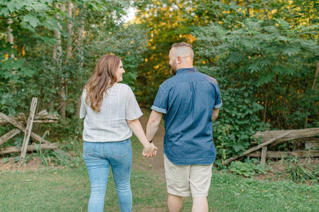 Hold hands look at each  other - Watson's Mill Engagement Session Manotick - Bright & Airy photography - Grey Loft Studio - Ottawa Wedding Photographer - Ottawa Wedding Videographer - Engagement Session Locations in Ottawa - Summer Engagement session - Light blue and Cream with casual jeans and strap sandals. Ottawa Photo Studio.