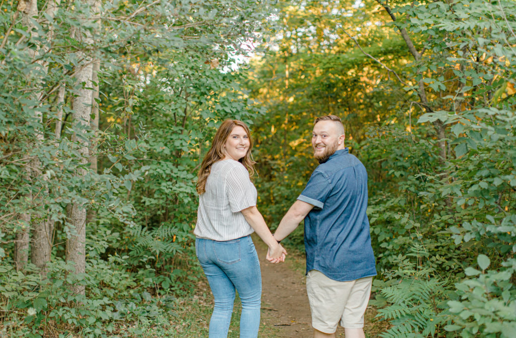 Hold hands look back at me! Watson's Mill Engagement Session Manotick - Bright & Airy photography - Grey Loft Studio - Ottawa Wedding Photographer - Ottawa Wedding Videographer - Engagement Session Locations in Ottawa - Summer Engagement session - Light blue and Cream with casual jeans and strap sandals. Ottawa Photo Studio.