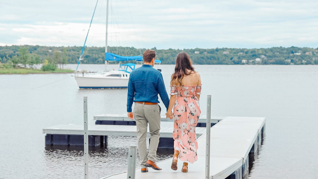Couple walking together on a dock -Ideas for what to wear for Engagement Photography, Modern Engagement Session Inspiration Wardrobe Ideas. Unsure of what to wear for your engagement photos, we've got you! Romantic white with Pink Flower dress for Summer Engagement in Ottawa. Grey Loft Studio is Ottawa's Wedding and Engagement Photographer for Real couples, showcasing photos that are modern, bright, and fun. Pinhey's Point Dunrobin.
