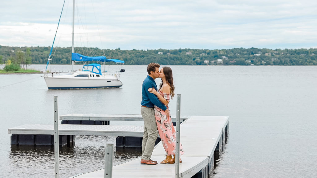 Couple kissing on a dock -Ideas for what to wear for Engagement Photography, Modern Engagement Session Inspiration Wardrobe Ideas. Unsure of what to wear for your engagement photos, we've got you! Romantic white with Pink Flower dress for Summer Engagement in Ottawa. Grey Loft Studio is Ottawa's Wedding and Engagement Photographer for Real couples, showcasing photos that are modern, bright, and fun. Pinhey's Point Dunrobin.