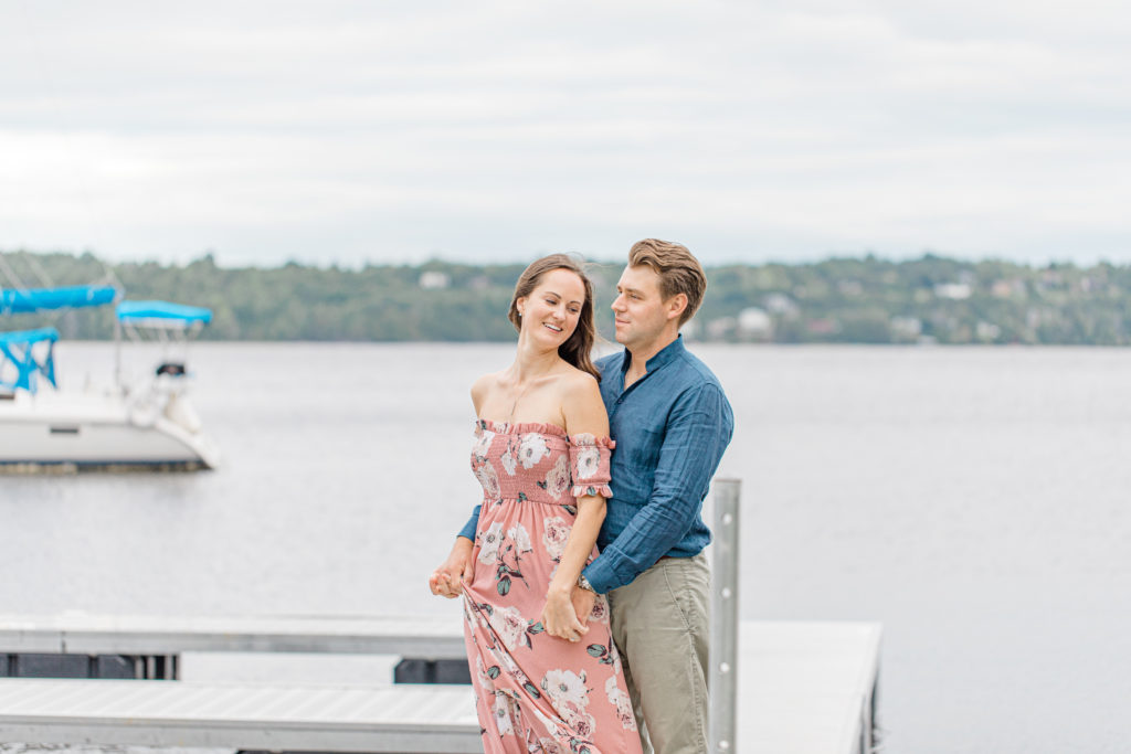 Couple posing near water-Ideas for what to wear for Engagement Photography, Modern Engagement Session Inspiration Wardrobe Ideas. Unsure of what to wear for your engagement photos, we've got you! Romantic white with Pink Flower dress for Summer Engagement in Ottawa. Grey Loft Studio is Ottawa's Wedding and Engagement Photographer for Real couples, showcasing photos that are modern, bright, and fun. Pinhey's Point Dunrobin. Light and Airy Photography Videography Team