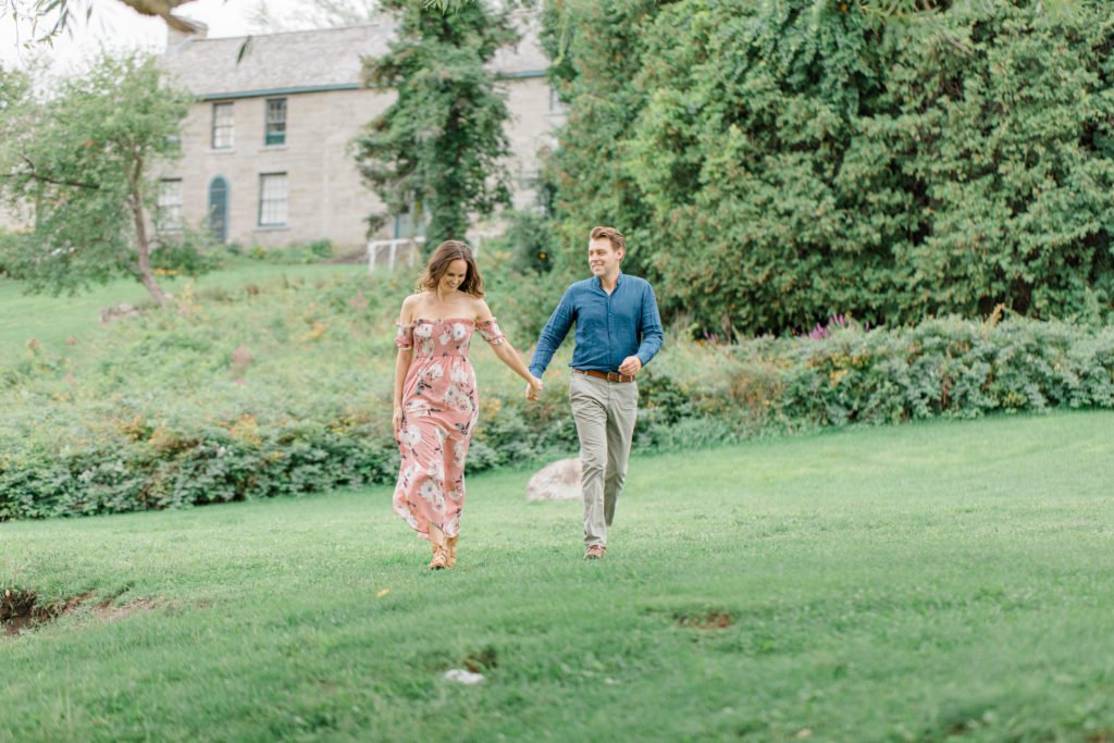Couple walking near large tree -Ideas for what to wear for Engagement Photography, Modern Engagement Session Inspiration Wardrobe Ideas. Unsure of what to wear for your engagement photos, we've got you! Romantic white with Pink Flower dress for Summer Engagement in Ottawa. Grey Loft Studio is Ottawa's Wedding and Engagement Photographer for Real couples, showcasing photos that are modern, bright, and fun. Pinhey's Point Dunrobin. Light and Airy Photography Videography Team