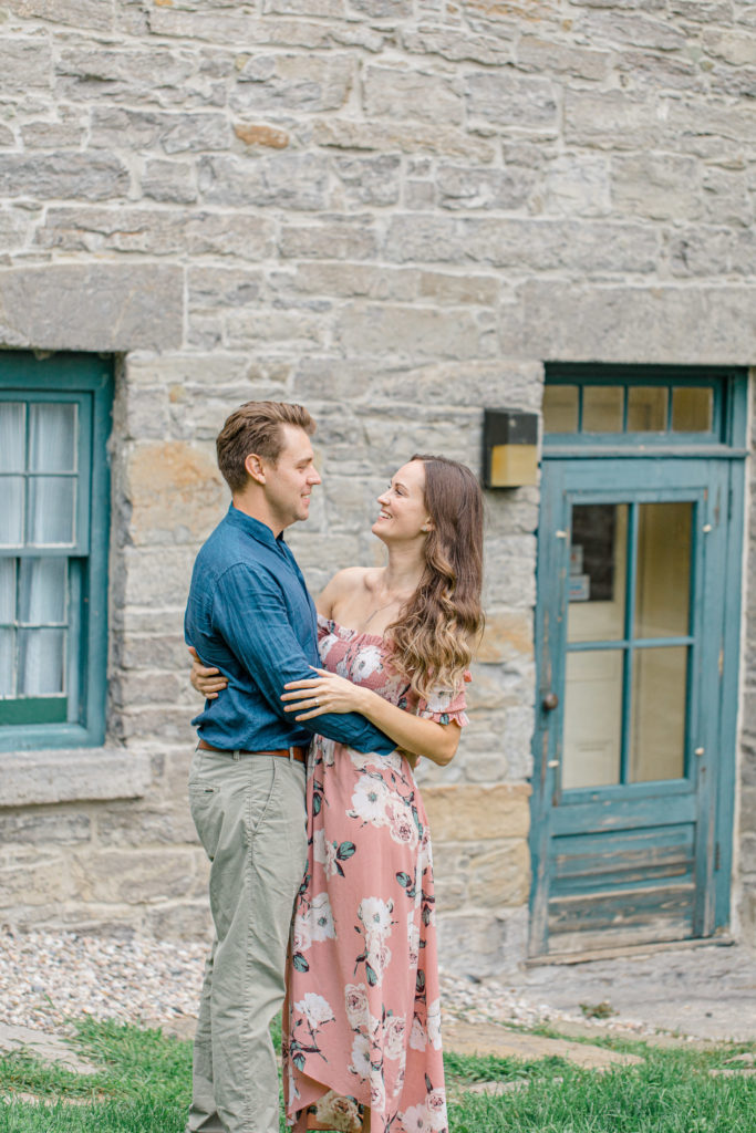 Couple smiling at each other -Ideas for what to wear for Engagement Photography, Modern Engagement Session Inspiration Wardrobe Ideas. Unsure of what to wear for your engagement photos, we've got you! Romantic white with Pink Flower dress for Summer Engagement in Ottawa. Grey Loft Studio is Ottawa's Wedding and Engagement Photographer for Real couples, showcasing photos that are modern, bright, and fun. Pinhey's Point Dunrobin.