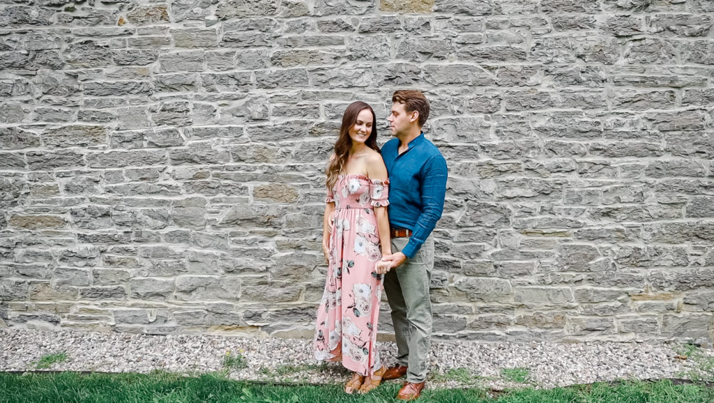 Standing in front of Brick Wall - Ideas for what to wear for Engagement Photography, Modern Engagement Session Inspiration Wardrobe Ideas. Unsure of what to wear for your engagement photos, we've got you! Romantic white with Pink Flower dress for Summer Engagement in Ottawa. Grey Loft Studio is Ottawa's Wedding and Engagement Photographer for Real couples, showcasing photos that are modern, bright, and fun. Pinhey's Point Dunrobin.